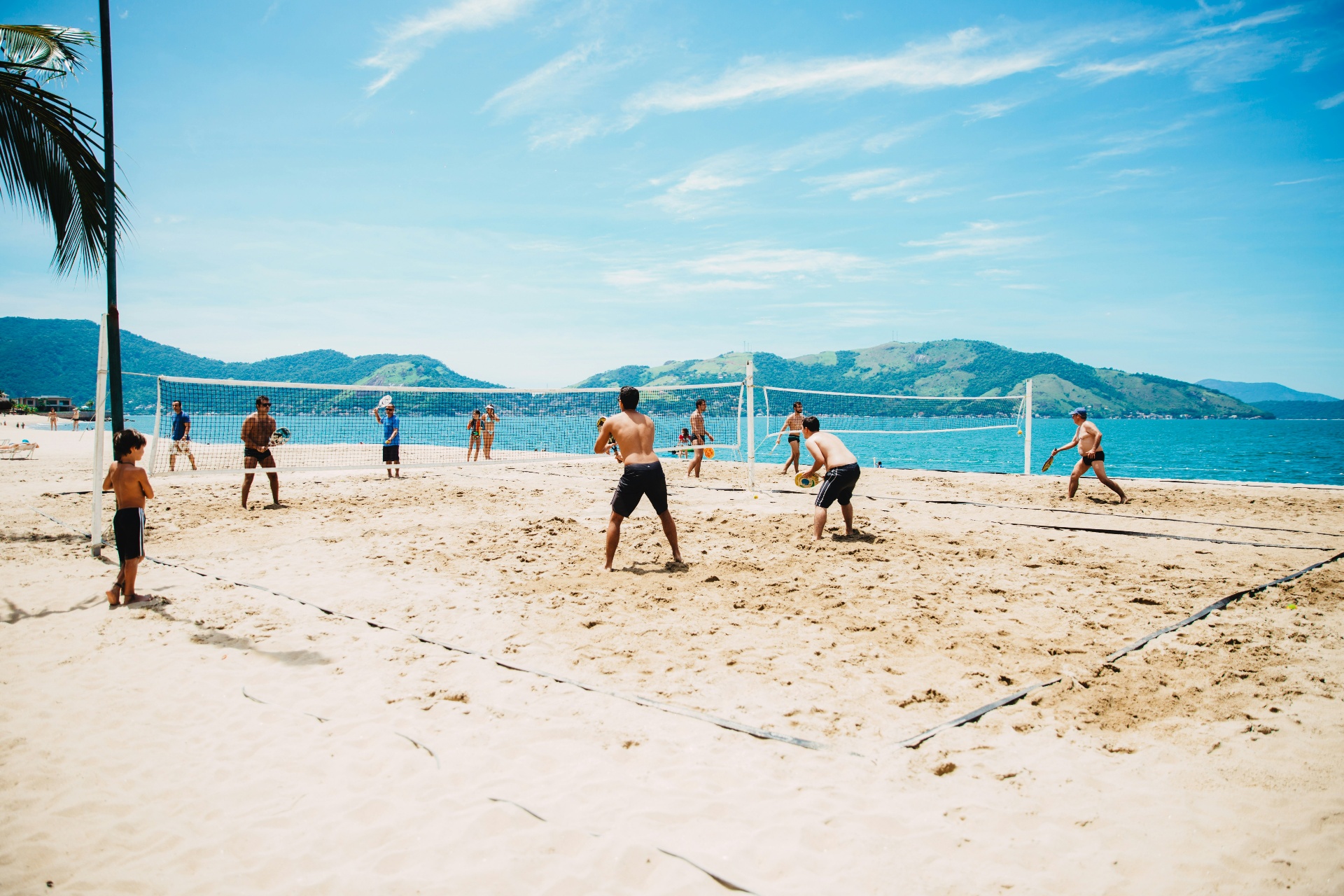 Players enjoying beach tennis on a sunny Brazilian beach with mountains and ocean in the background