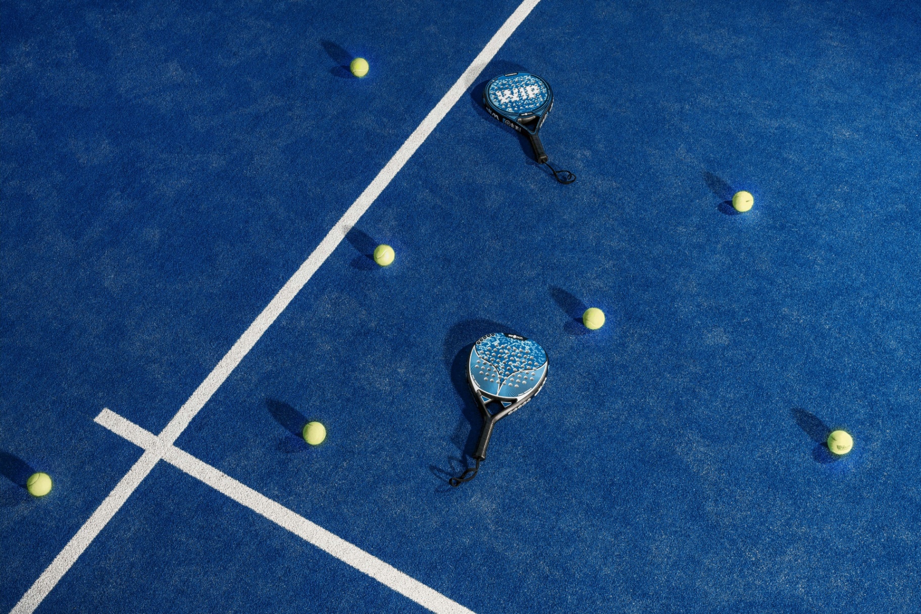 Aerial view of a blue padel court with two paddles and scattered yellow balls