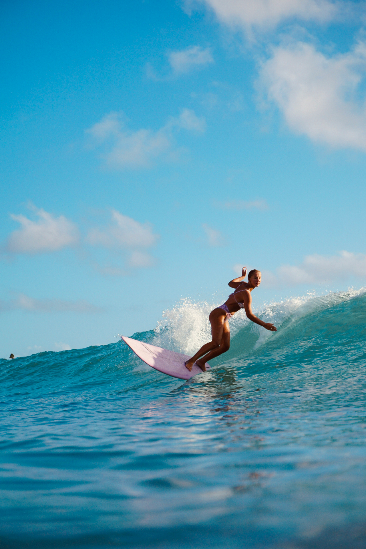 Female surfer riding a turquoise wave under a blue sky