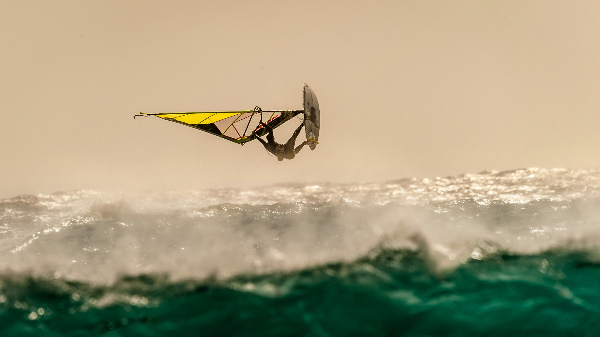 Windsurfer gliding across the ocean at sunset